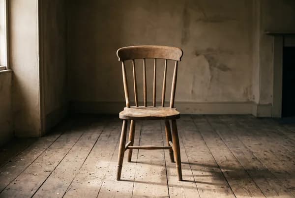 A single empty oak chair at the centre of a bare room, its worn seat and the dust on the floorboards catching the light while the rest of the room stays in soft shadow.